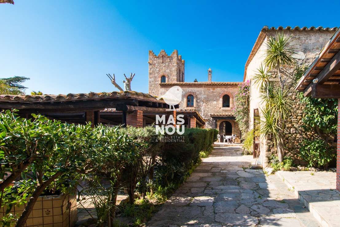 Un encantador camino de piedra conduce a rústicos edificios de piedra y a una torre histórica, perfecta para quienes buscan comprar hoteles en España.