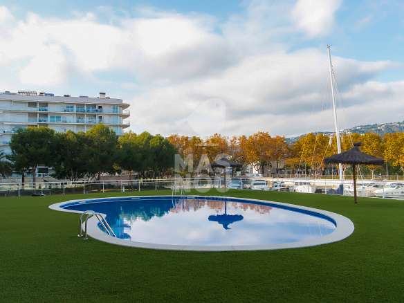Descubra una piscina ovalada al aire libre con escalera metálica, situada en un frondoso césped cerca de barcos y elegantes pisos en Port d'Aro.