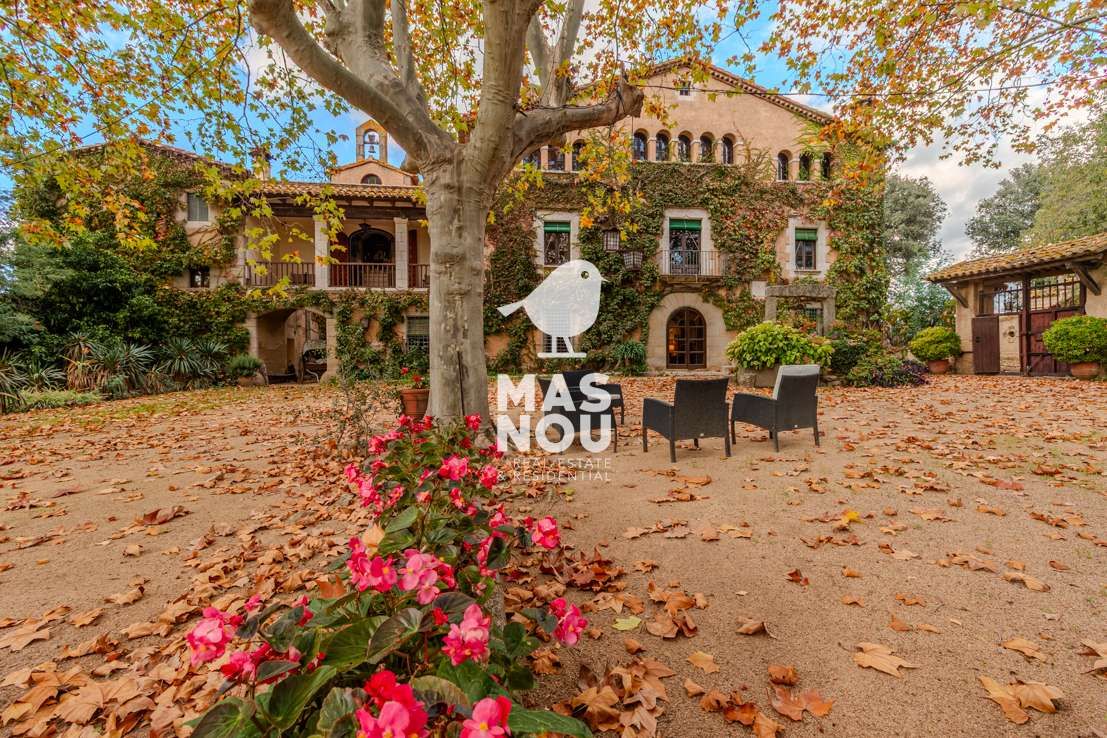 Experimente el encanto de una finca histórica cubierta de hiedra, con balcones, hojas otoñales, flores en flor y dos sillas negras.
